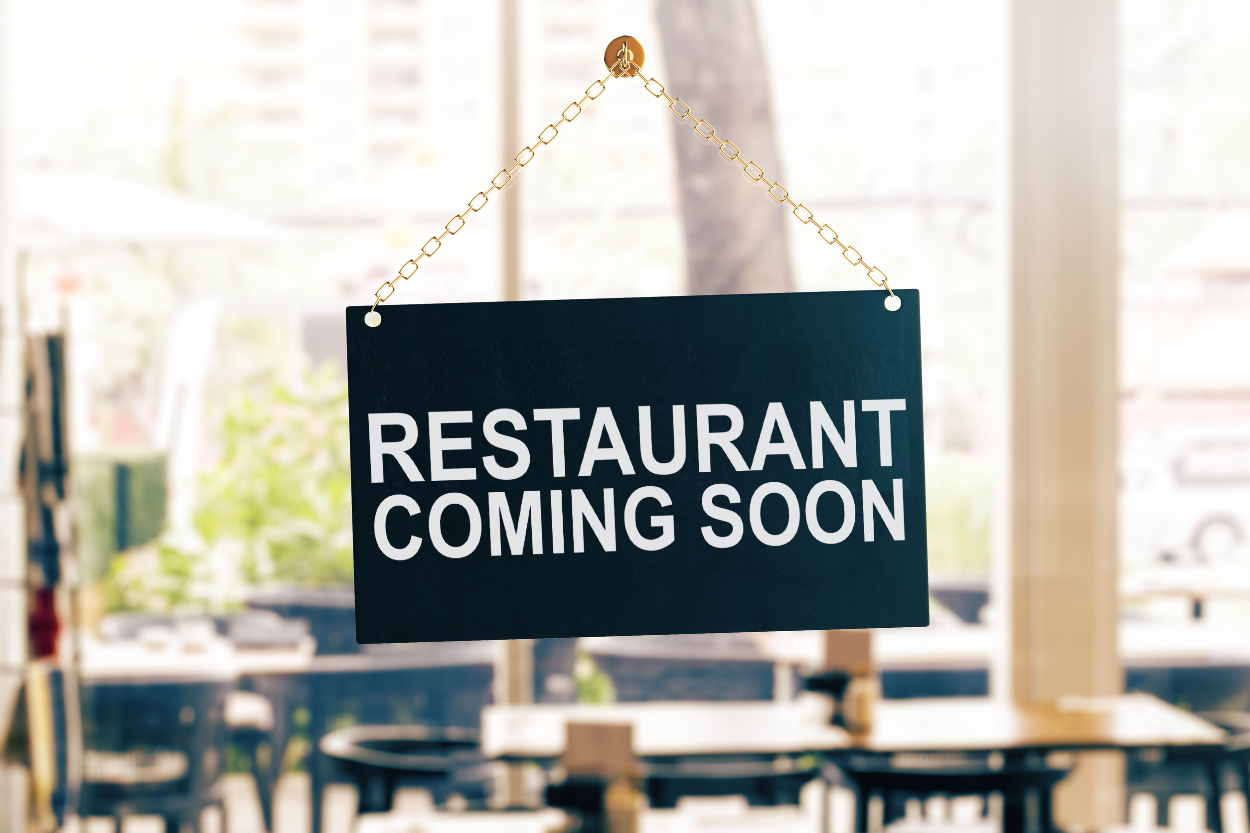 Sign hanging on glass window that reads "Restaurant Coming Soon"