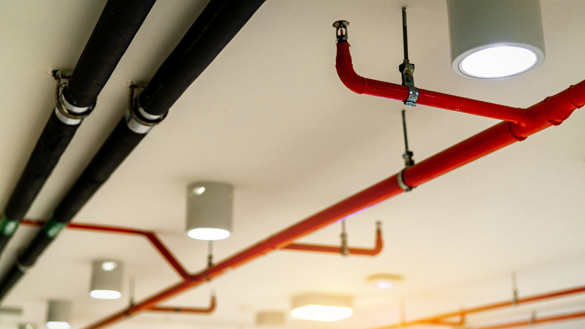 Fire sprinkler system with red pipes hanging from ceiling inside building.